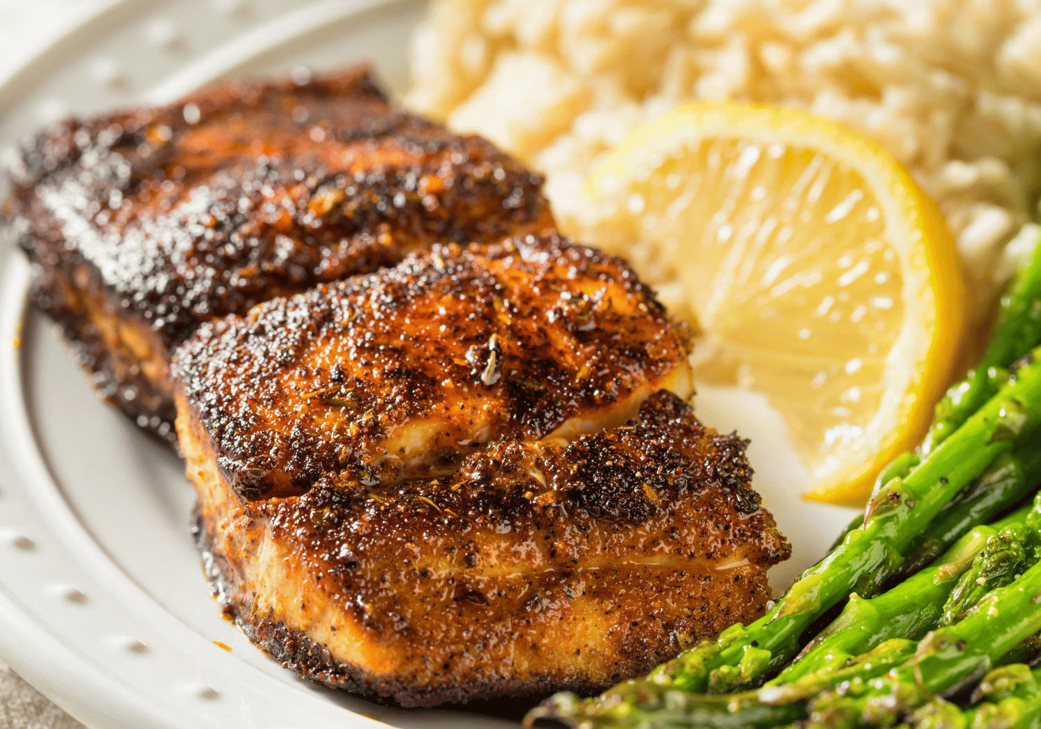 Grilled chicken with crispy skin, lemon wedge, asparagus, and rice on a white plate.